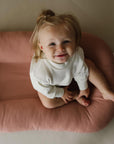 Smiling toddler sitting inside a pink organic cotton baby lounger