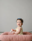 Baby sitting on the edge of a Gumdrop pink infant lounger holding a toy