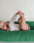 Baby lying on a Moss green lounger cover, playing with feet