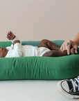 Newborn lying in a Moss green infant lounger beside a parent on the floor