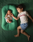 Toddler lying next to a baby in a Moss green infant lounger, overhead view