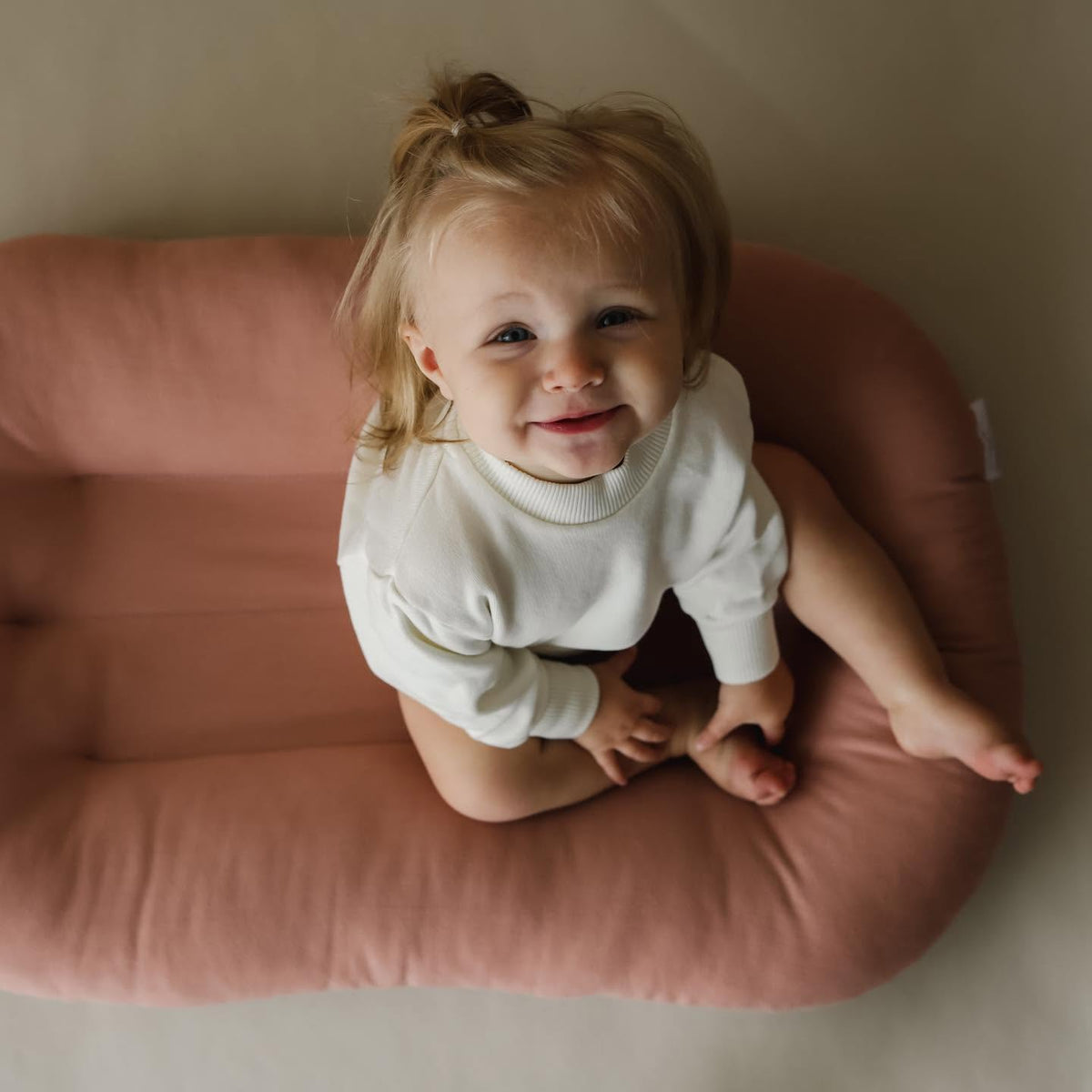 Smiling toddler sitting inside a pink organic cotton baby lounger