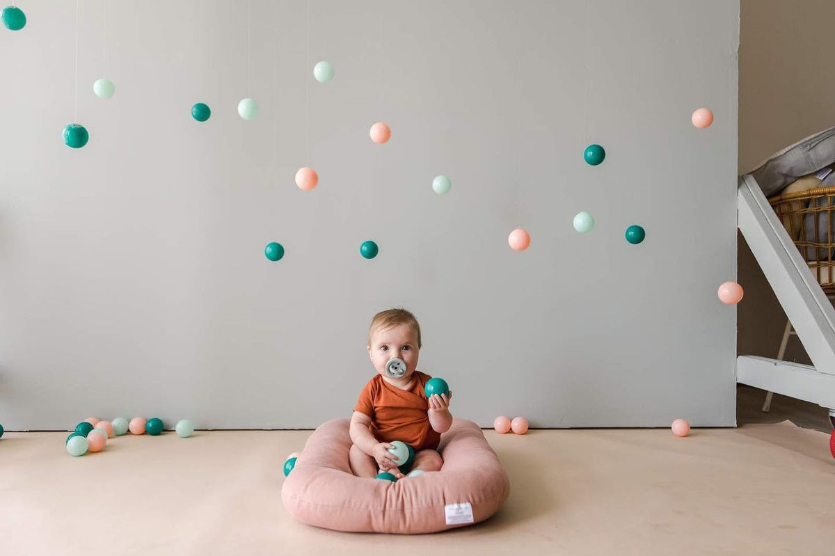 Baby lounging in a pink infant lounger in a bright playroom