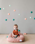 Baby lounging in a pink infant lounger in a bright playroom