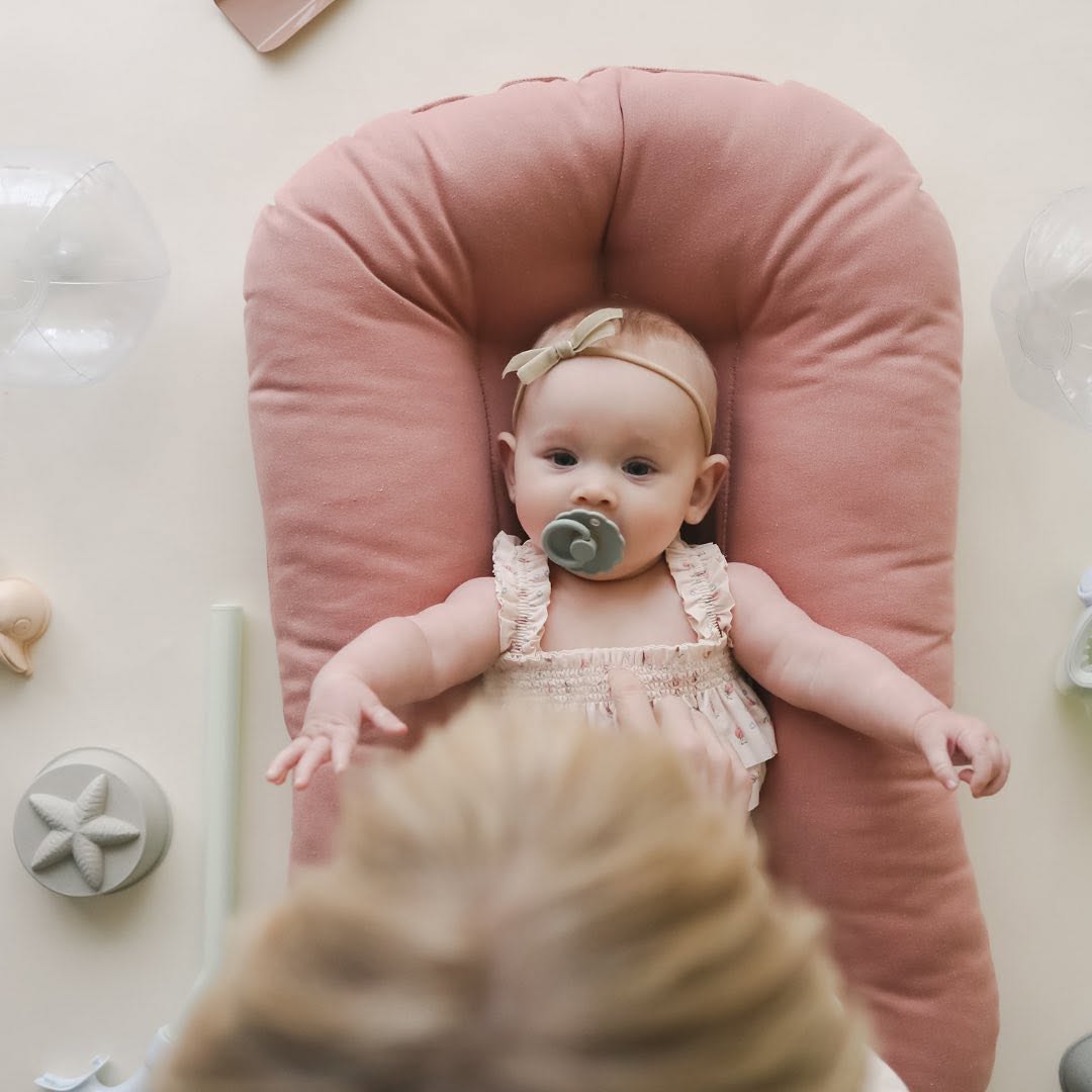 Baby with a pacifier lying in a lounger with a Gumdrop pink cover