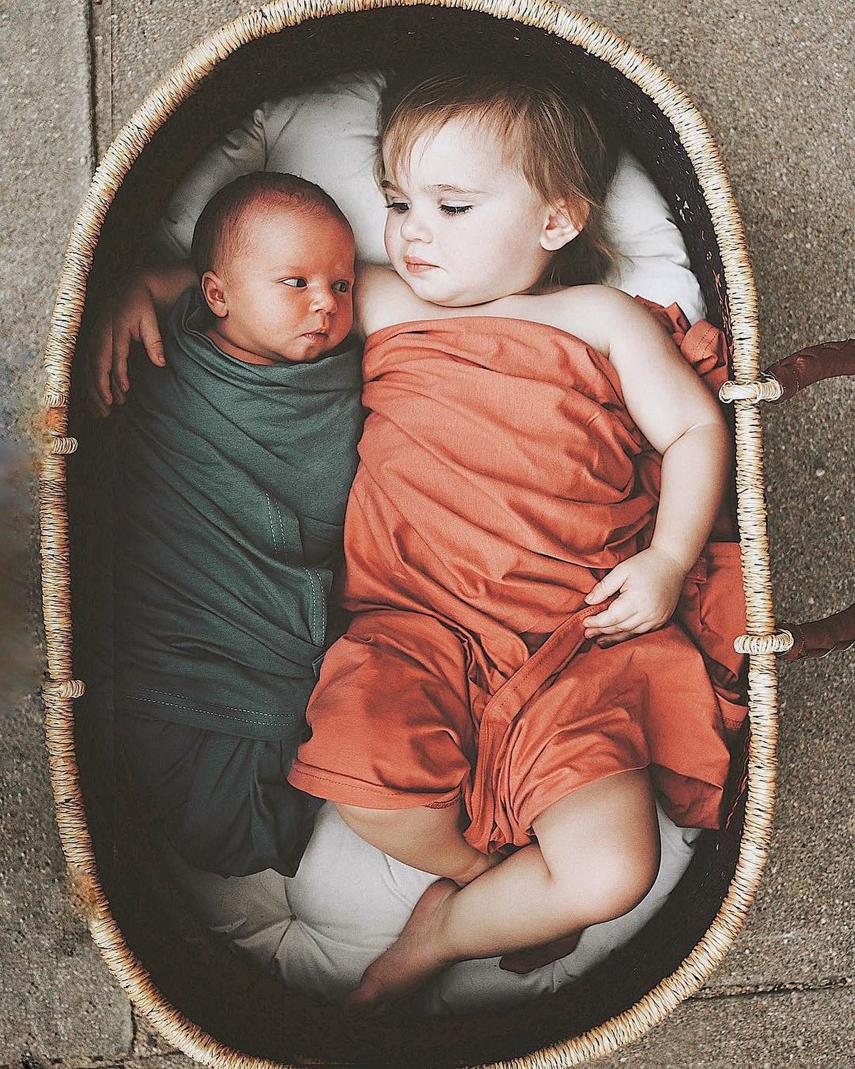 Newborn and toddler resting together in a woven basket