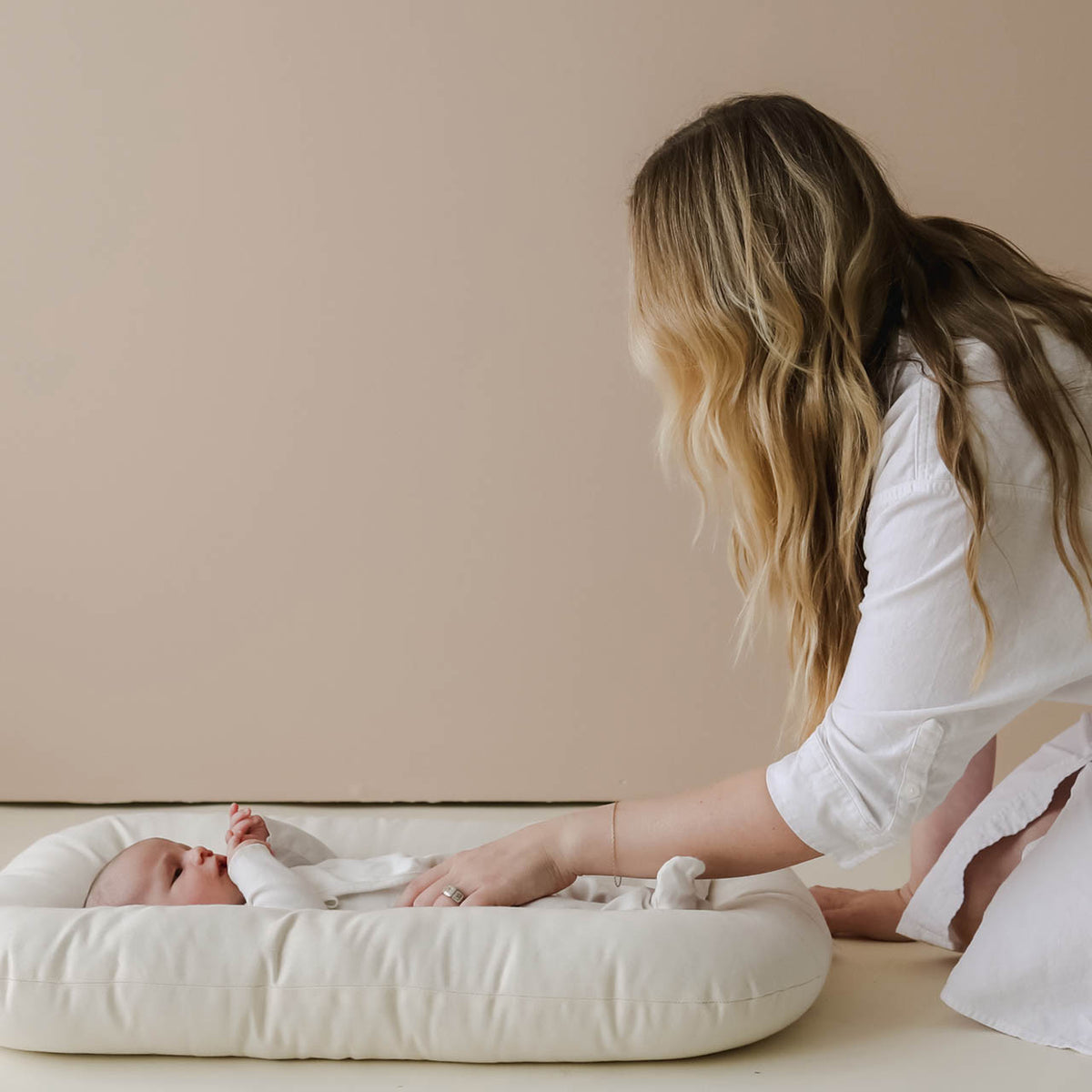 Parent tending to a baby lying in a lounger with a Natural cover