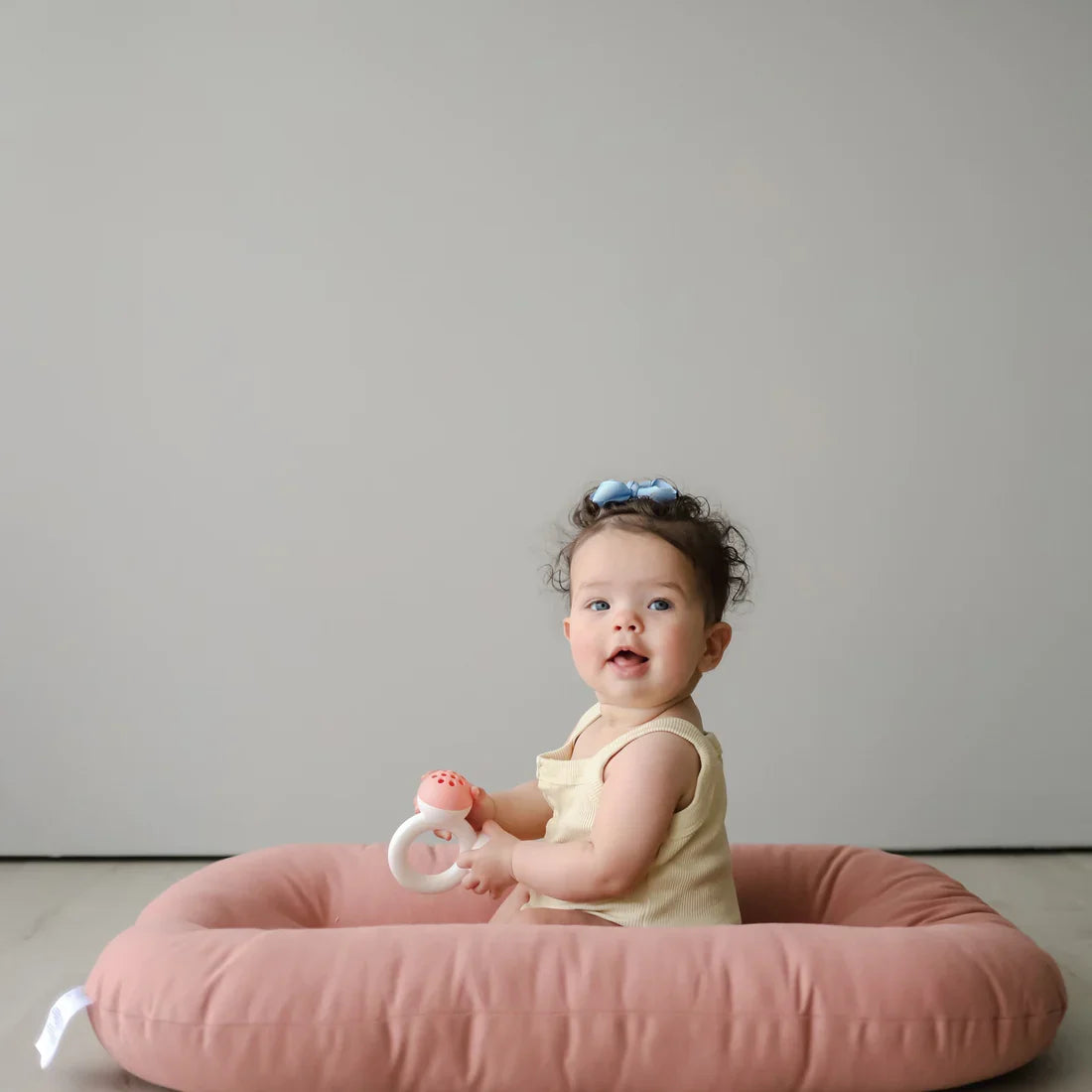 Baby sitting on the edge of a Gumdrop pink infant lounger holding a toy
