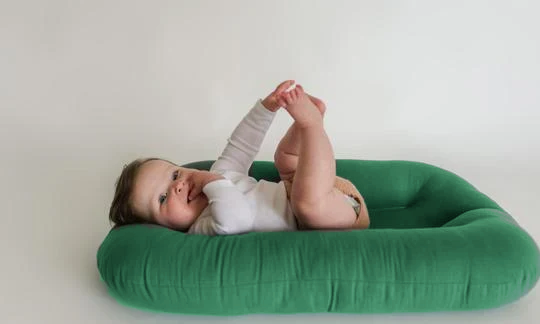 Baby lying on a Moss green lounger cover, playing with feet
